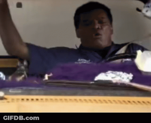 A Man In A Blue Shirt Is Sitting In Front Of A Purple And White Item GIF