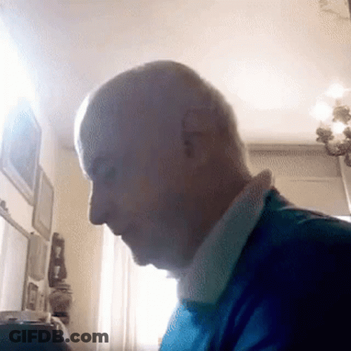 A Man In A Blue Shirt Is Sitting In Front Of A Window . GIF