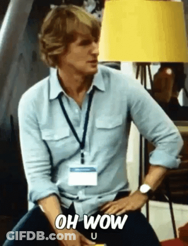 A Man In A Blue Shirt Is Sitting In Front Of A Yellow Lamp And Says Oh Wow GIF
