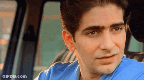 A Man In A Blue Shirt Is Sitting In The Back Seat Of A Car And Looking At The Camera . GIF