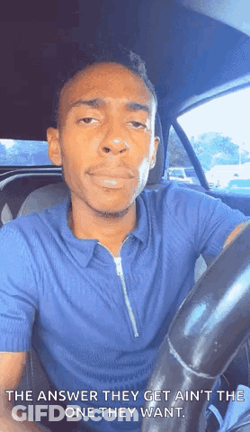 A Man In A Blue Shirt Is Sitting In The Driver 'S Seat Of A Car And Making A Face . GIF