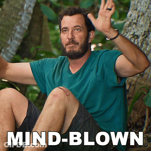 A Man In A Blue Shirt Is Sitting In The Woods With The Words Mind-Blown Behind Him GIF