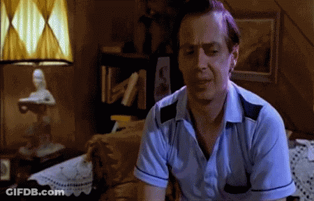 A Man In A Blue Shirt Is Sitting On A Bed In A Dark Room GIF