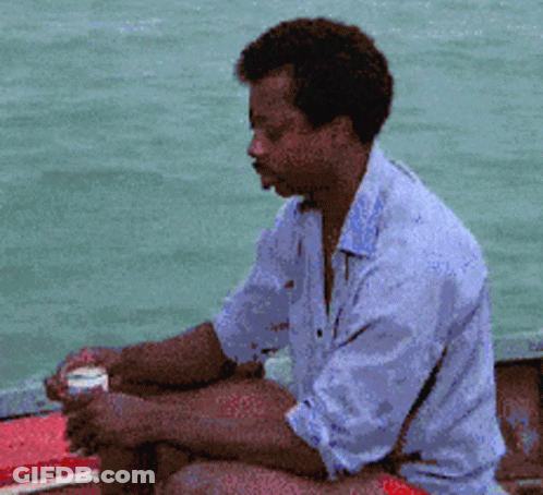 A Man In A Blue Shirt Is Sitting On A Boat Looking At The Water GIF