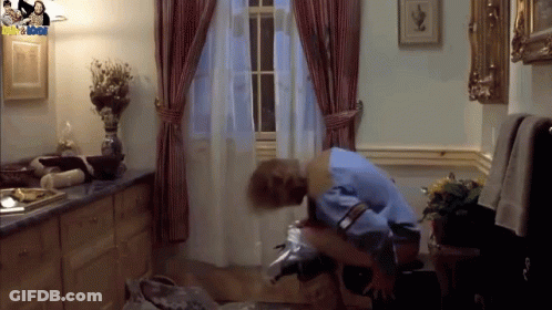 A Man In A Blue Shirt Is Sitting On A Chair In A Room With A Picture Of A Man And A Woman On The Wall GIF