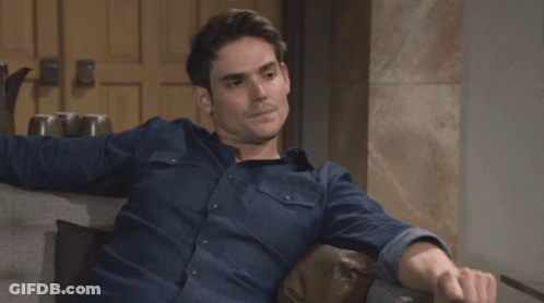 A Man In A Blue Shirt Is Sitting On A Chair GIF