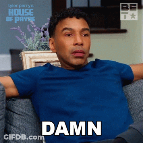 A Man In A Blue Shirt Is Sitting On A Couch And Saying " Damn " GIF