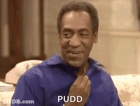 A Man In A Blue Shirt Is Sitting On A Couch And Smiling While Holding His Hand To His Chest . GIF