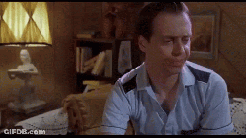 A Man In A Blue Shirt Is Sitting On A Couch In A Living Room . GIF