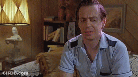 A Man In A Blue Shirt Is Sitting On A Couch In A Living Room With His Eyes Closed . GIF