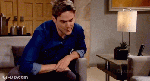 A Man In A Blue Shirt Is Sitting On A Couch In Front Of A Lamp That Says Global GIF
