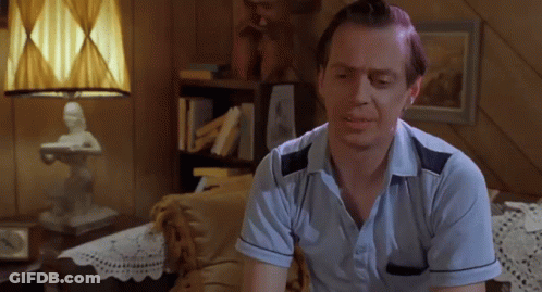 A Man In A Blue Shirt Is Sitting On A Couch In Front Of A Lamp GIF