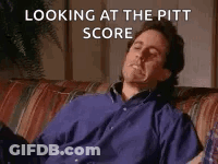A Man In A Blue Shirt Is Sitting On A Couch With His Eyes Closed And Looking At The Pitt Score . GIF