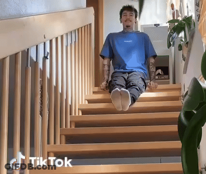 A Man In A Blue Shirt Is Sitting On A Set Of Wooden Stairs With Tiktok Written On The Bottom Right GIF