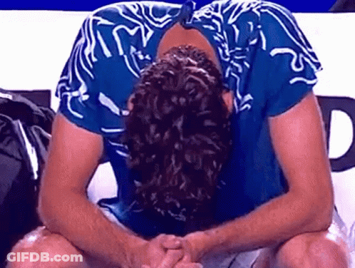 A Man In A Blue Shirt Is Sitting With His Head Down And His Hands Folded . GIF