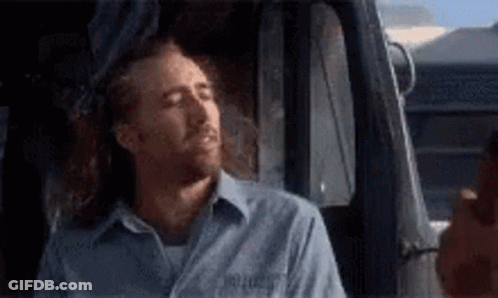 A Man In A Blue Shirt Is Sleeping In A Truck . GIF