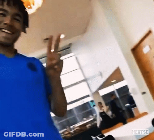 A Man In A Blue Shirt Is Smiling And Giving A Peace Sign GIF