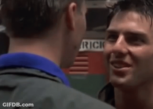 A Man In A Blue Shirt Is Smiling And Looking At The Camera In A Room . GIF