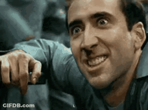 A Man In A Blue Shirt Is Smiling And Pointing At Something . GIF