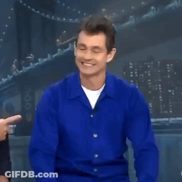 A Man In A Blue Shirt Is Smiling And Pointing At The Camera GIF