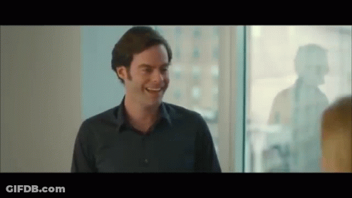 A Man In A Blue Shirt Is Smiling And Talking To Another Man In Front Of A Window . GIF