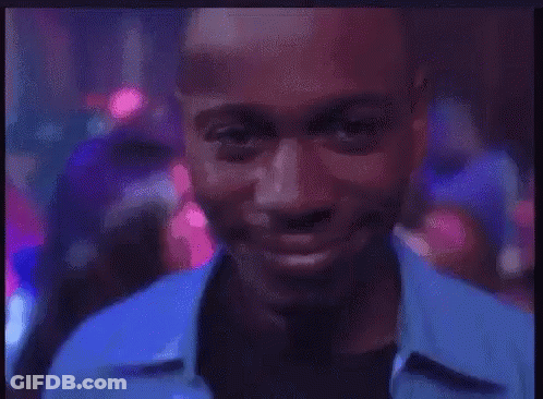 A Man In A Blue Shirt Is Smiling In A Club GIF