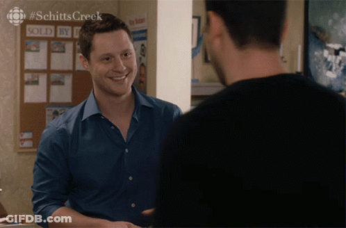 A Man In A Blue Shirt Is Smiling In Front Of A Sold By Sign GIF