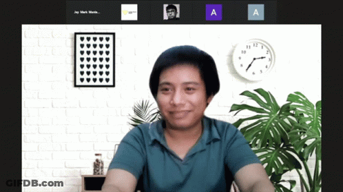 A Man In A Blue Shirt Is Smiling In Front Of A Wall With A Clock That Says 10:08 GIF
