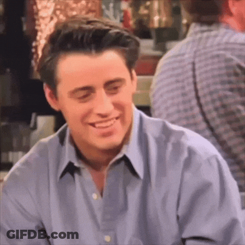 A Man In A Blue Shirt Is Smiling While Sitting In A Bar . GIF