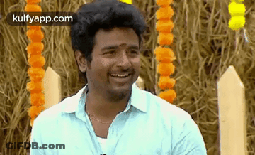 A Man In A Blue Shirt Is Smiling While Standing In Front Of A Pile Of Hay . GIF