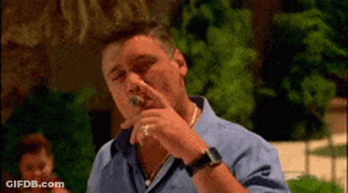 A Man In A Blue Shirt Is Smoking A Cigar Outdoors GIF
