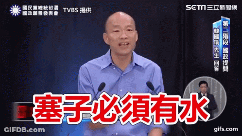 A Man In A Blue Shirt Is Speaking Into A Microphone With Chinese Writing On It GIF