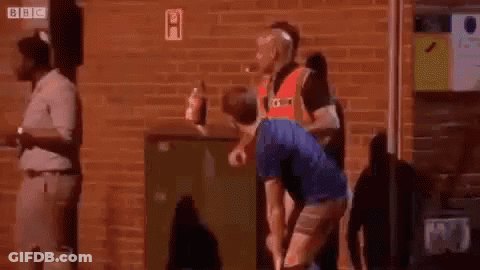 A Man In A Blue Shirt Is Squatting Down In Front Of A Brick Wall . GIF
