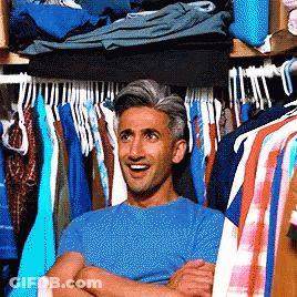 A Man In A Blue Shirt Is Standing In A Closet Full Of Clothes GIF