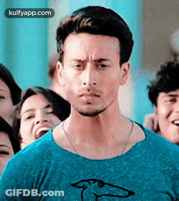 A Man In A Blue Shirt Is Standing In A Crowd Of People . GIF