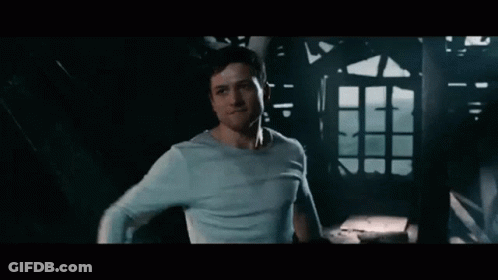 A Man In A Blue Shirt Is Standing In A Dark Room Looking At Something . GIF