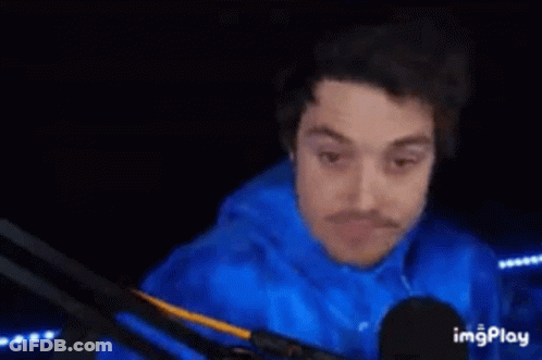 A Man In A Blue Shirt Is Standing In A Dark Room With His Hands Behind His Back . GIF