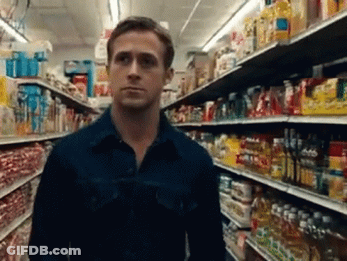 A Man In A Blue Shirt Is Standing In A Grocery Store Aisle Looking At Something GIF