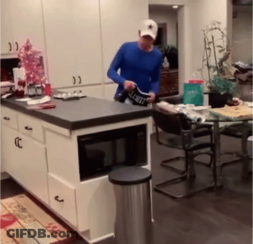 A Man In A Blue Shirt Is Standing In A Kitchen Holding A Shirt That Says Limit GIF