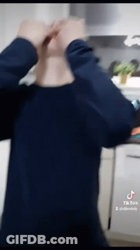 A Man In A Blue Shirt Is Standing In A Kitchen With His Hands On His Head GIF