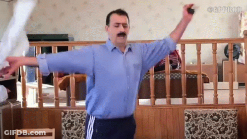 A Man In A Blue Shirt Is Standing In A Living Room With His Arms Outstretched .. GIF