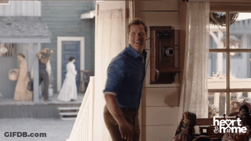 A Man In A Blue Shirt Is Standing In A Room With A Heart And Frame Logo GIF