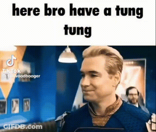 A Man In A Blue Shirt Is Standing In A Room With A Sign That Says `` Here Bro Have A Tung Tung '' . GIF