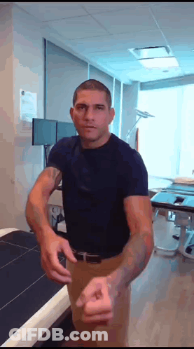 A Man In A Blue Shirt Is Standing In A Room With His Arms Outstretched GIF