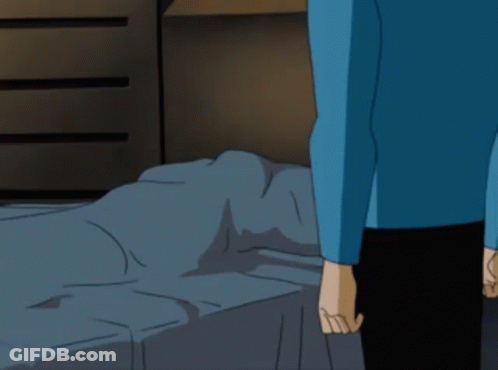 A Man In A Blue Shirt Is Standing In Front Of A Bed GIF