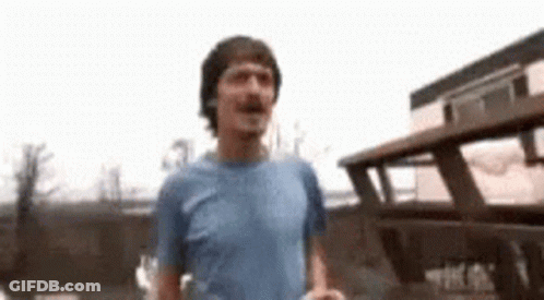 A Man In A Blue Shirt Is Standing In Front Of A Broken Down Bus . GIF