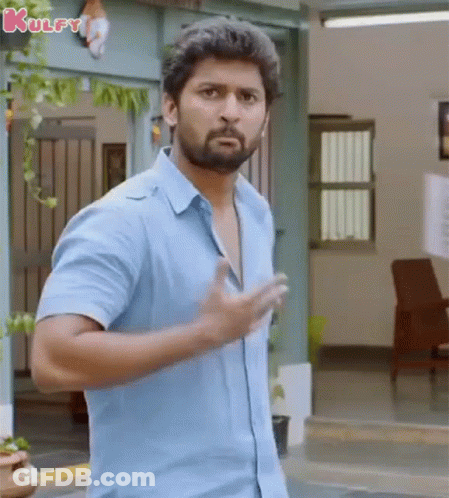 A Man In A Blue Shirt Is Standing In Front Of A Building And Making A Funny Face . GIF