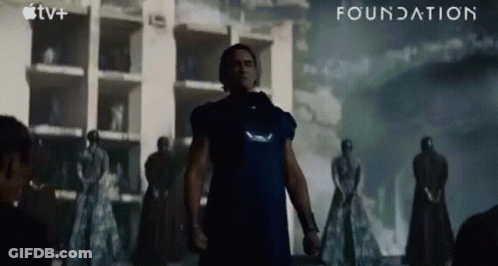 A Man In A Blue Shirt Is Standing In Front Of A Building With The Word Foundation Written On The Bottom GIF
