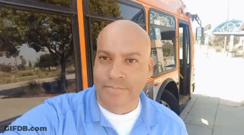 A Man In A Blue Shirt Is Standing In Front Of A Bus With The Number 8 On The Side GIF