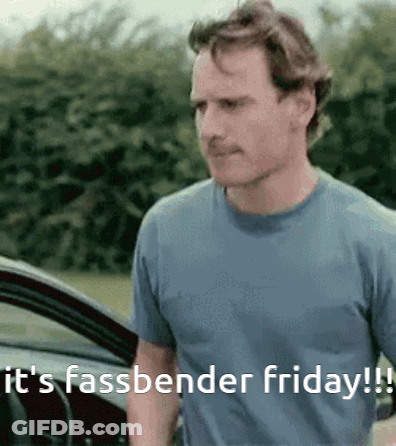A Man In A Blue Shirt Is Standing In Front Of A Car And Says It 'S Fassbender Friday ! GIF